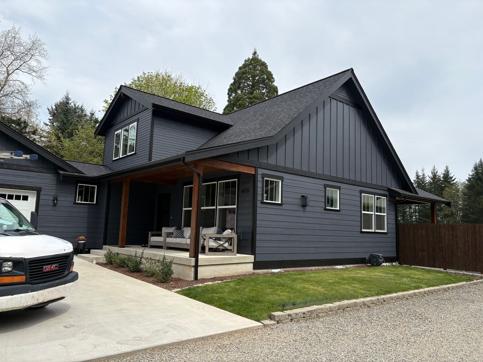 Modern dark-gray house with a front porch, driveway, and parked car in a suburban yard