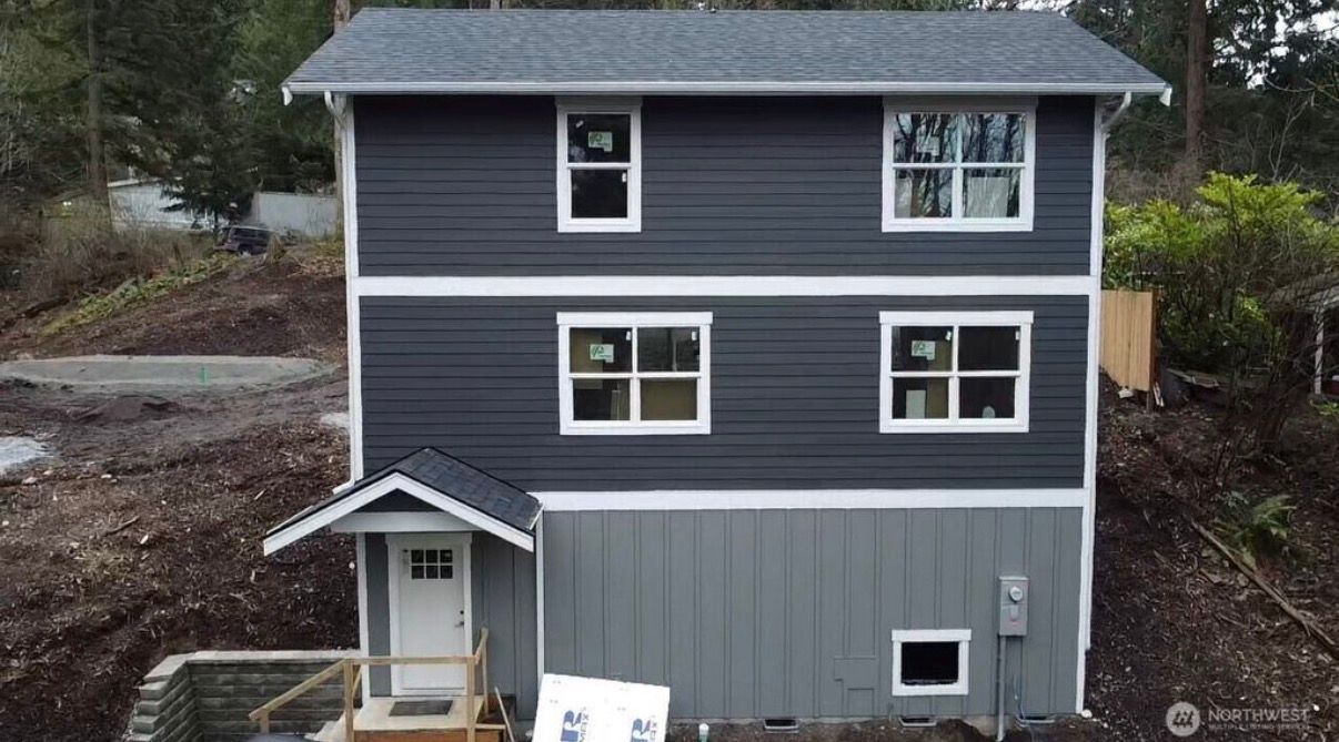 Three-story gray house with white trim and a small front porch, viewed from the yard