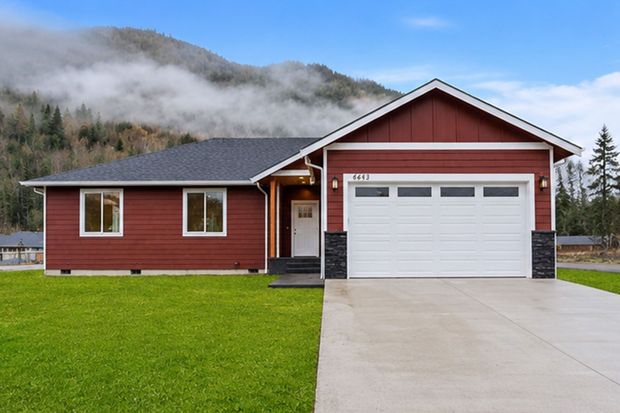 Red house with white garage door and concrete driveway in a misty mountainous setting