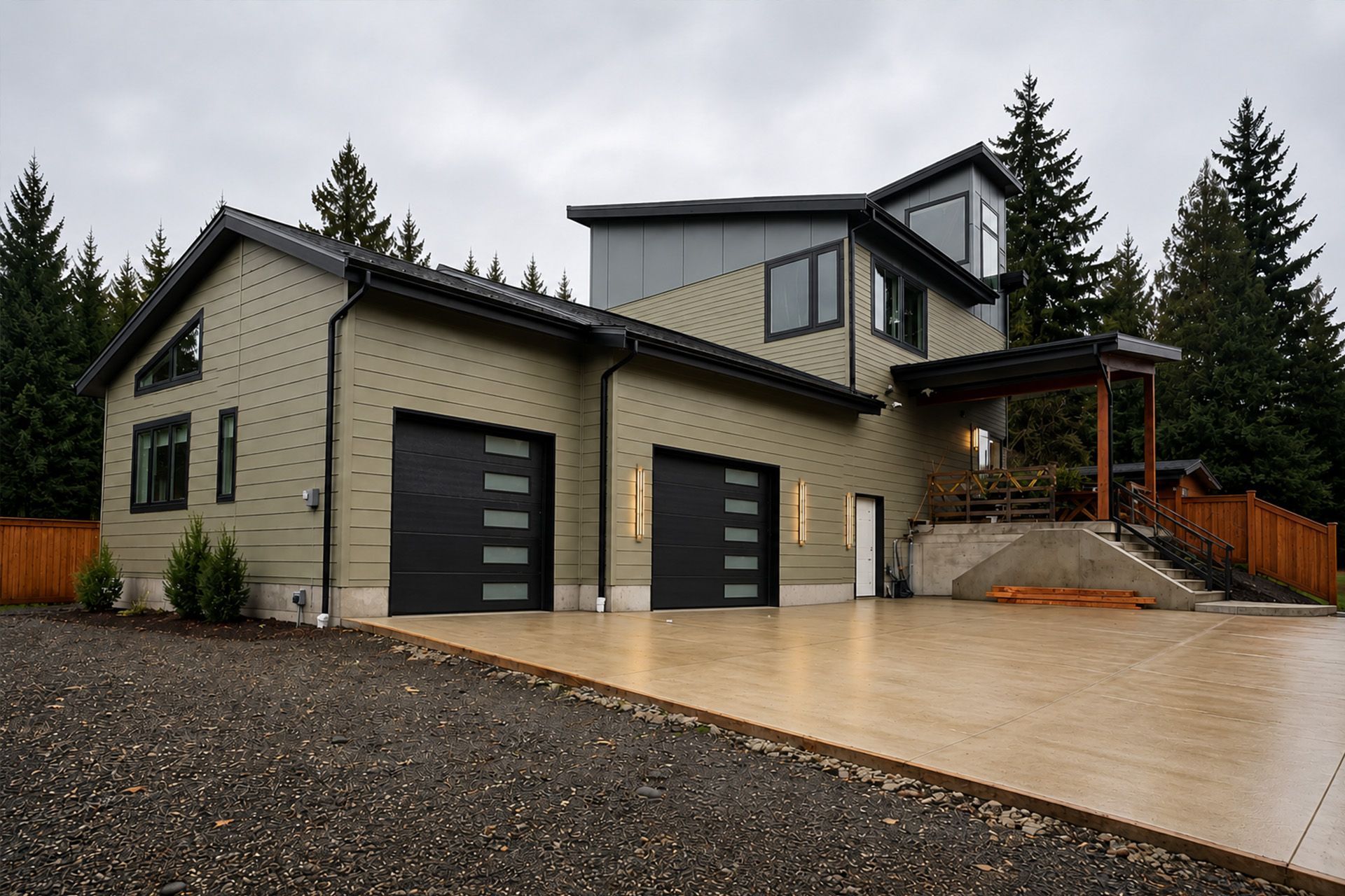 Modern gray house with two garage doors and a wet driveway on an overcast day
