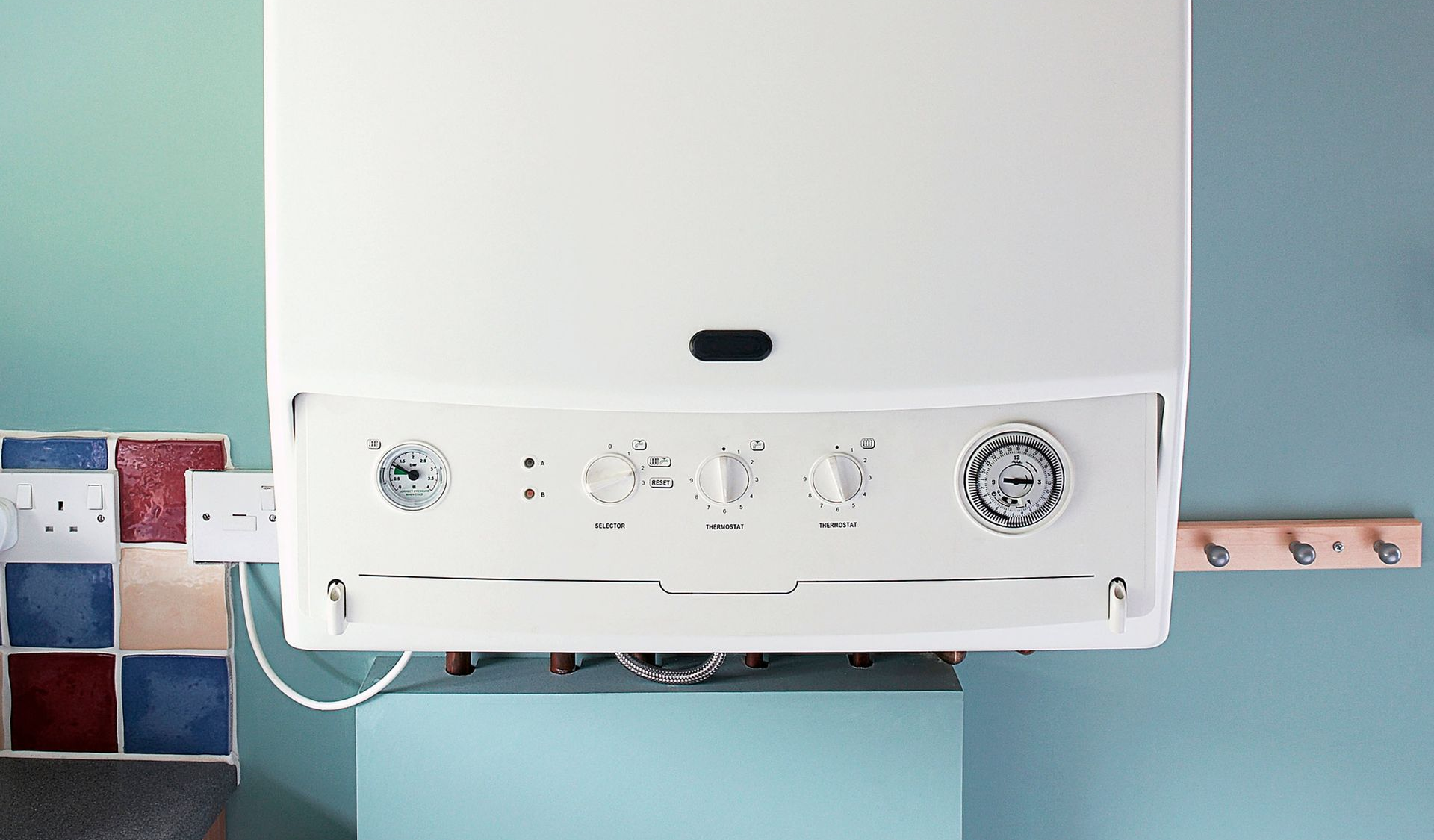 White wall-mounted gas boiler on a teal wall, with controls and a tile backsplash visible.