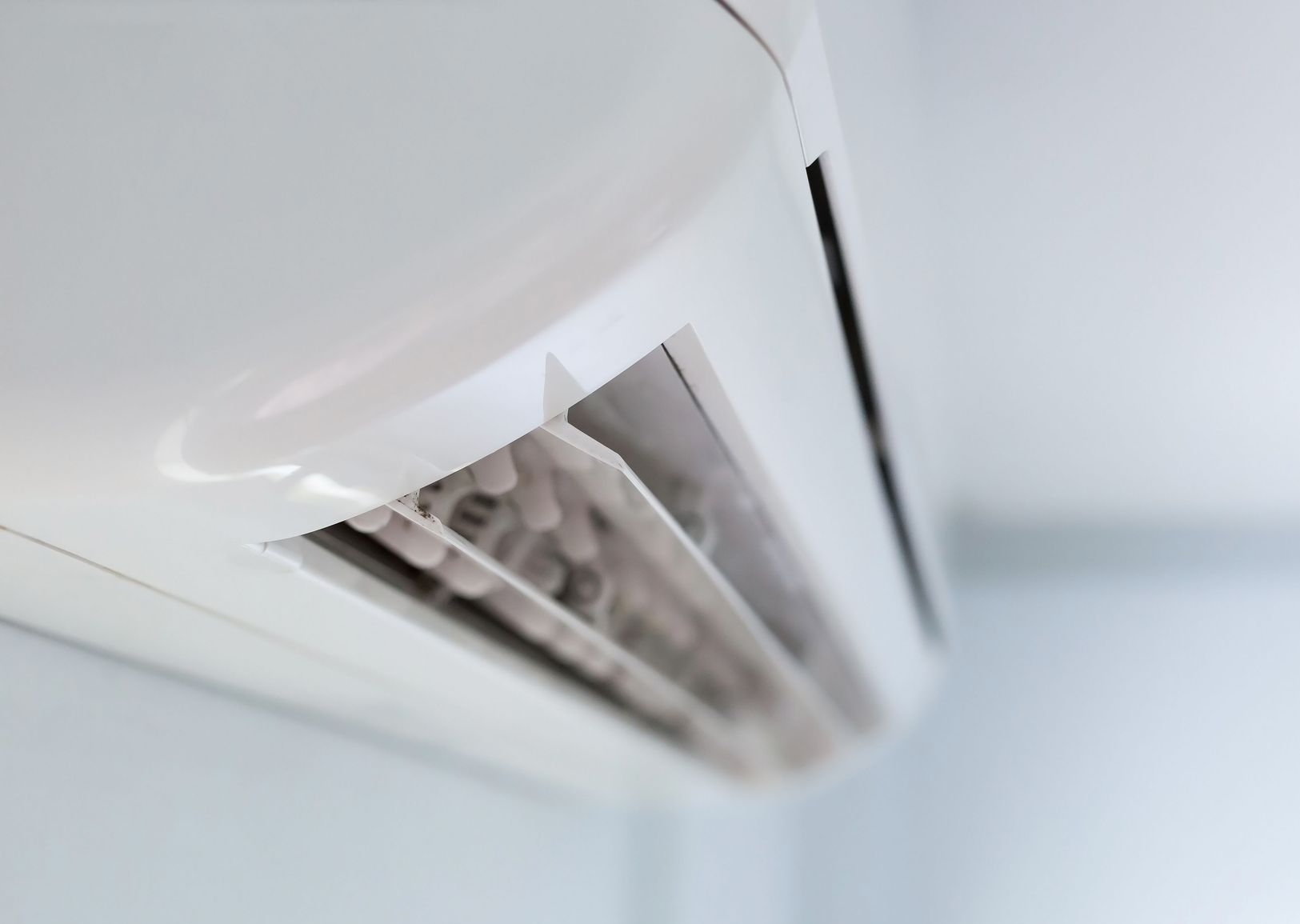 White wall-mounted air conditioner, angled, against a light blue wall.