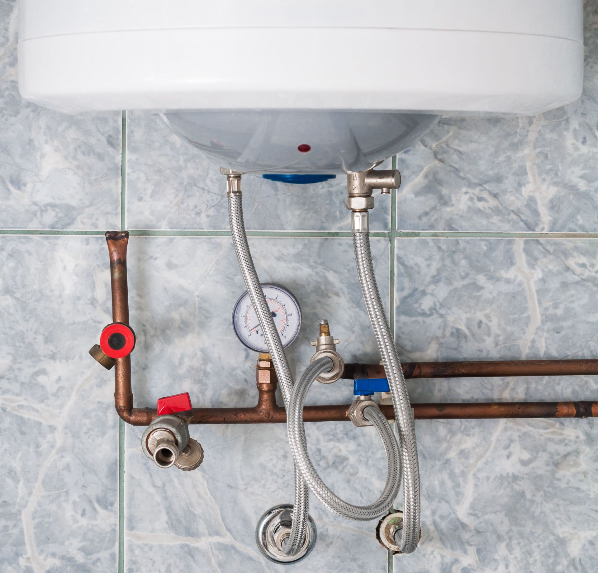 Water heater with copper pipes, pressure gauge, and control valves against a blue tile wall.