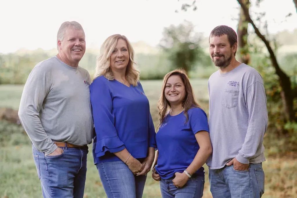 Family of four smiles, standing outdoors. Wearing blue shirts and jeans.