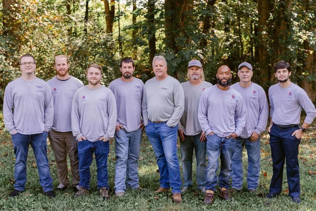 Three women in blue shirts and jeans sit on porch steps with pumpkins.