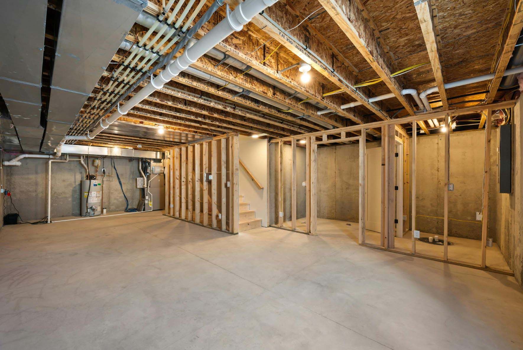 Unfinished basement with concrete floor, exposed wooden framing, pipes, and electrical wiring.