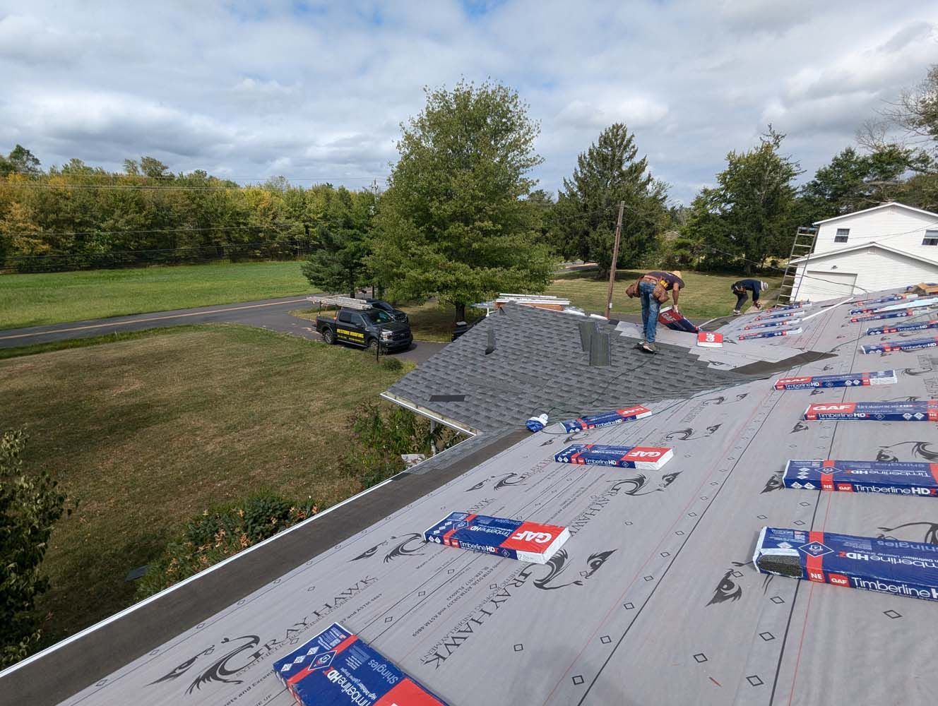 Roofers installing shingles on a house roof. Grey roofing underlayment visible with packs of shingles. Overcast day.