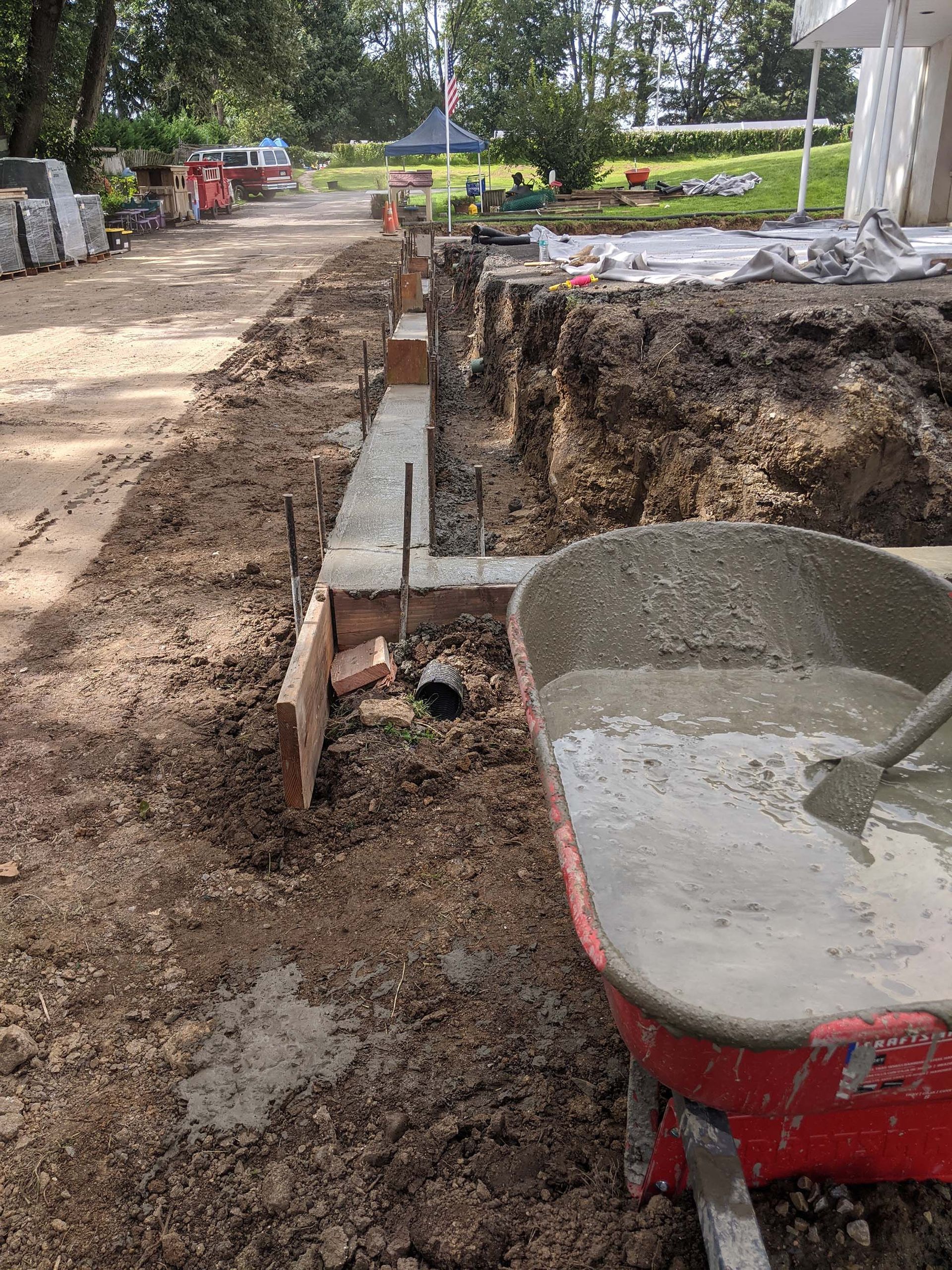 Construction site with concrete forms, wheelbarrow of wet concrete, and excavated soil.