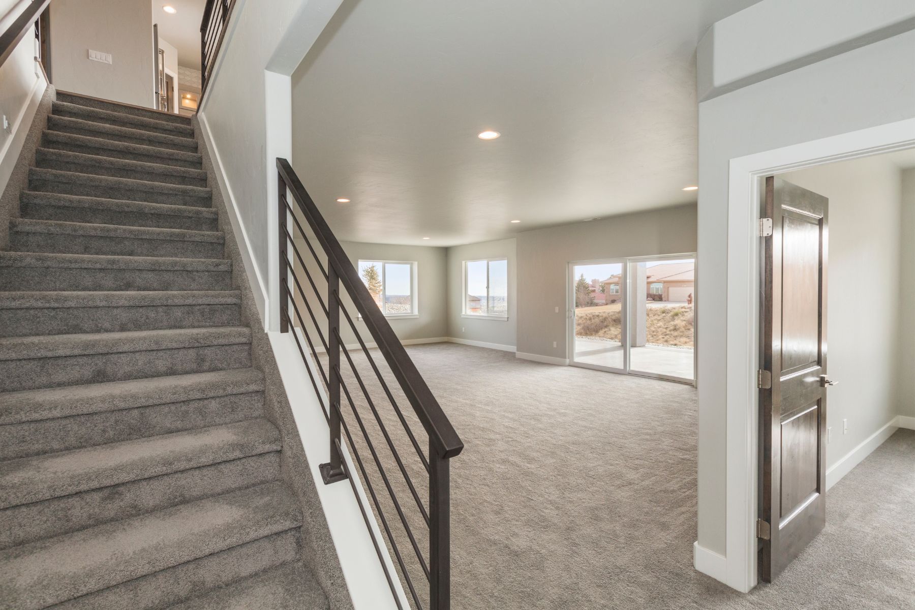 Staircase with gray carpet leads down to a room with light gray walls, large windows, and a doorway.