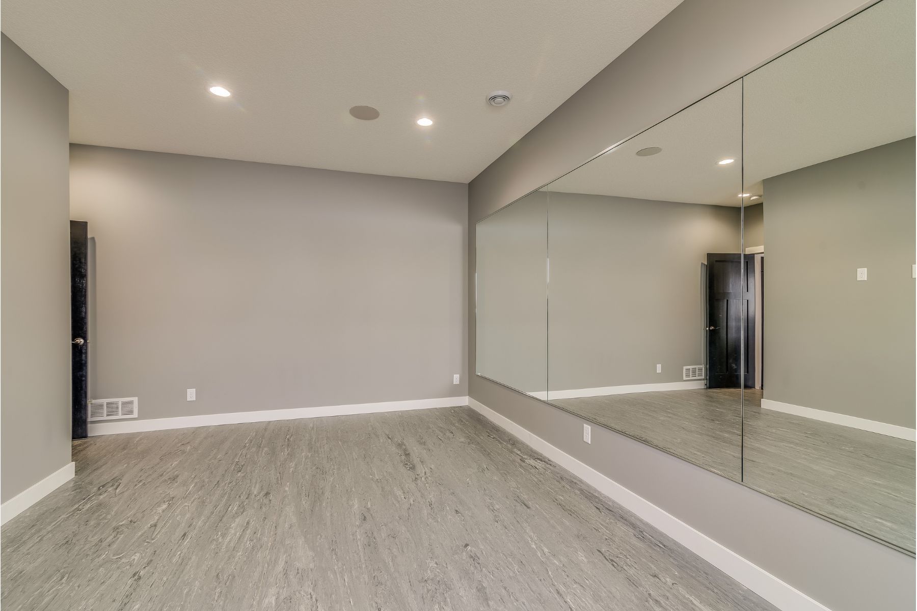 Empty dance studio with gray walls, large mirrors, and gray flooring.