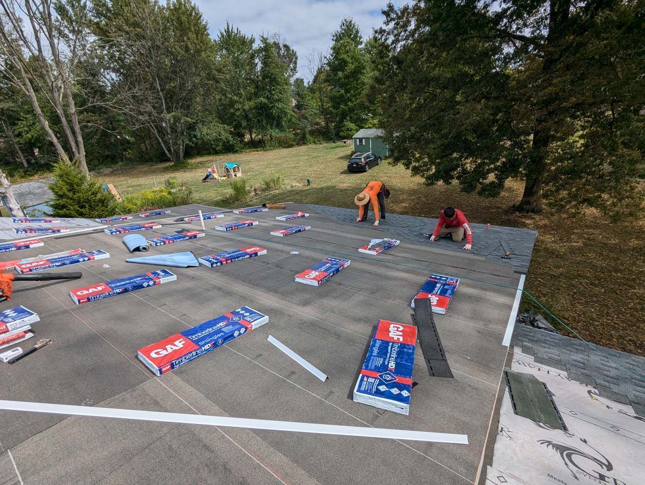 Workers installing roofing shingles on a low-slope roof outdoors on a sunny day.