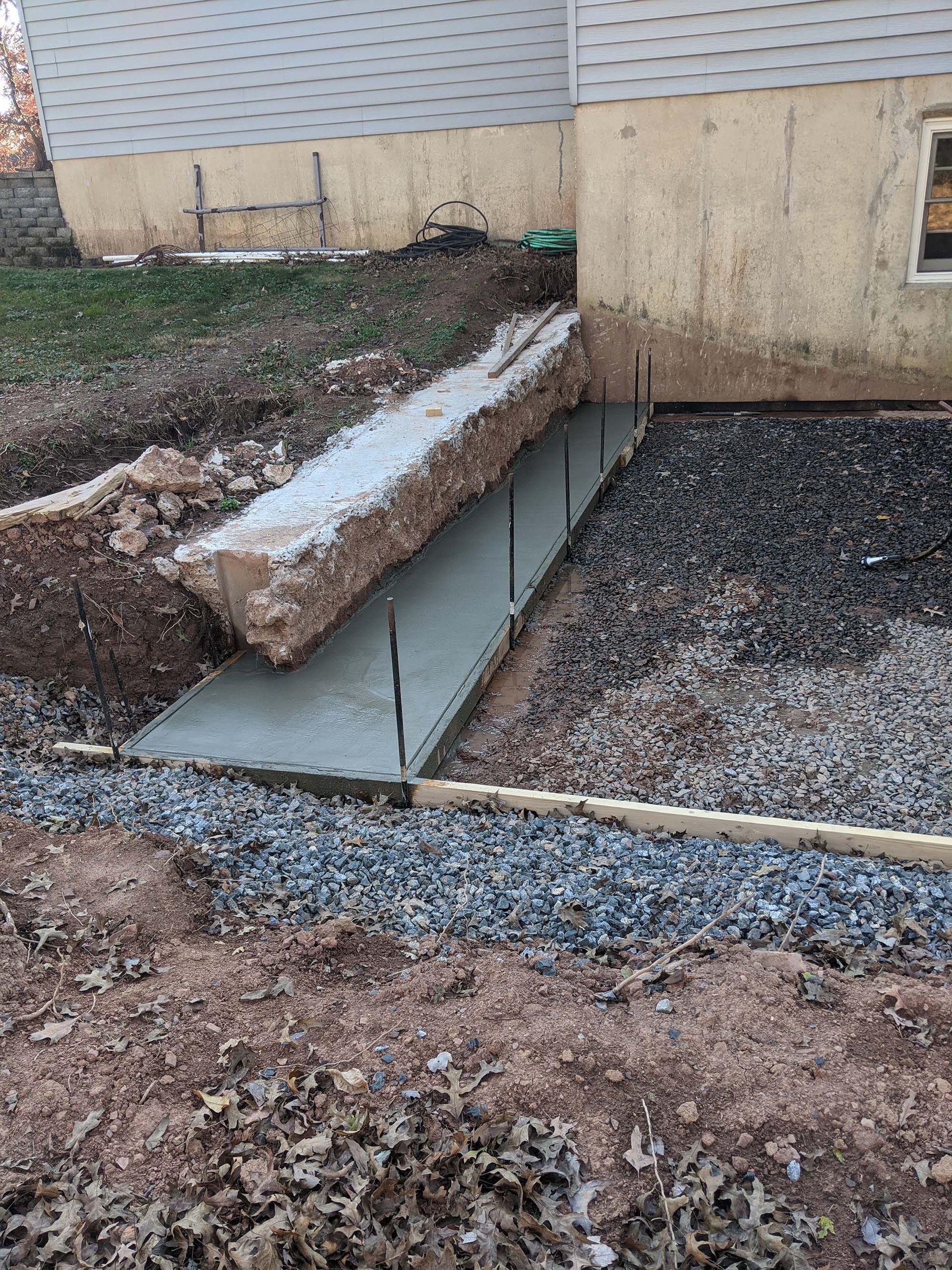 Freshly poured concrete ramp and landing next to a building, with exposed rebar and gravel edging.