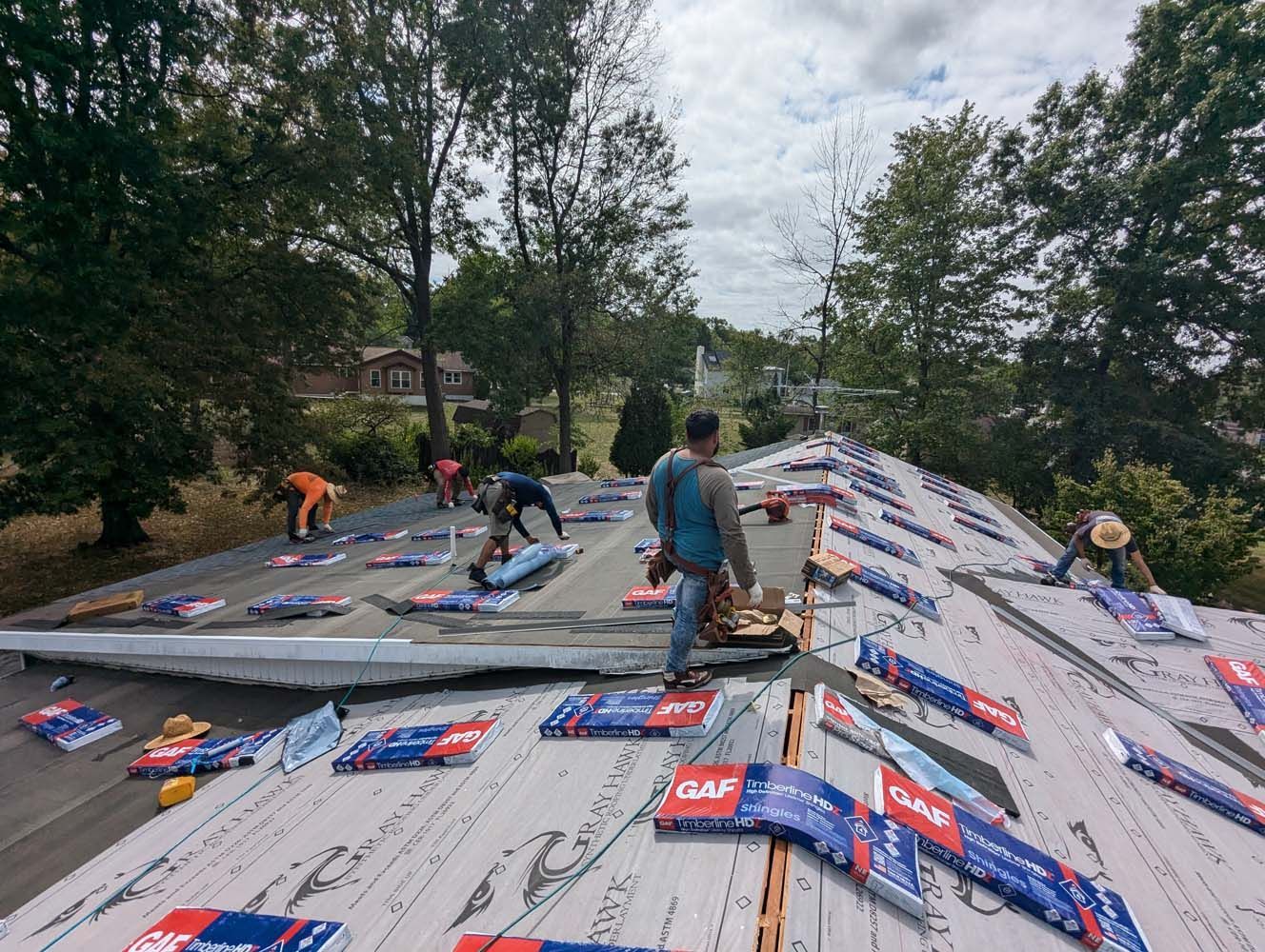 Roofers installing shingles on a house roof on a cloudy day.