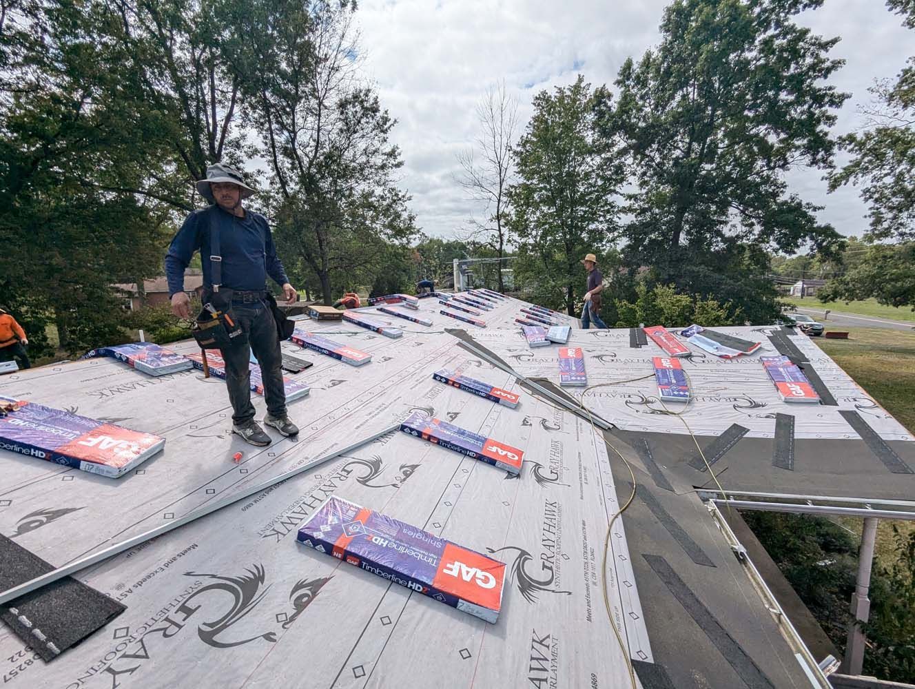 Roofers installing shingles on a house roof on a cloudy day.