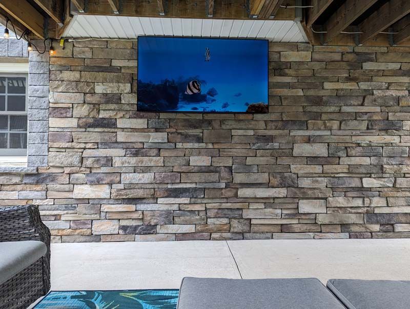 Large TV mounted on a stone wall, under a covered patio. Shows underwater scene.