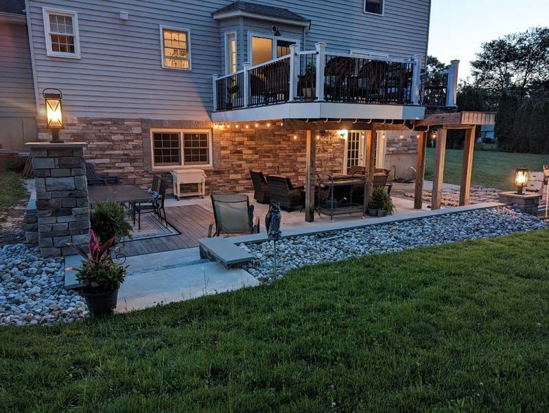 Backyard deck with string lights, stone columns, patio furniture, and grassy lawn.