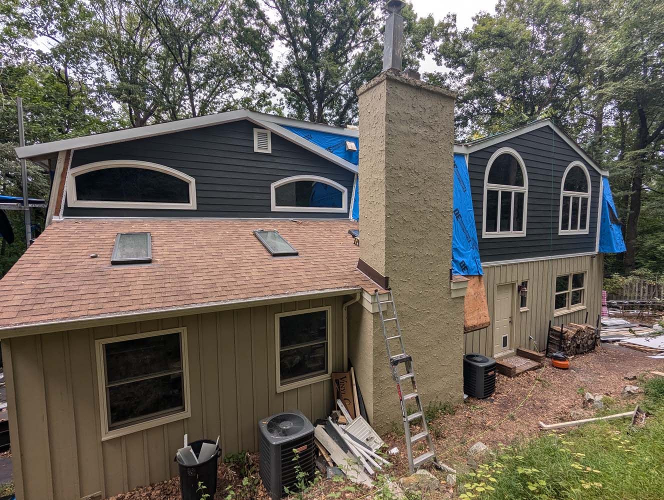 House with chimney, undergoing roof repairs; dark siding, blue tarp, ladder.