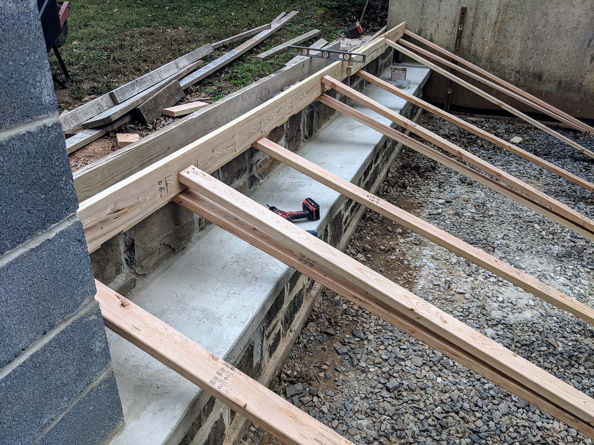 Wooden rafters being constructed over a cinder block wall, outdoors.