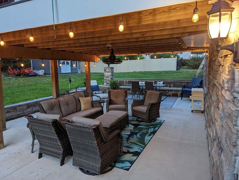 Patio with seating under a wooden pergola, string lights, and a stone wall.
