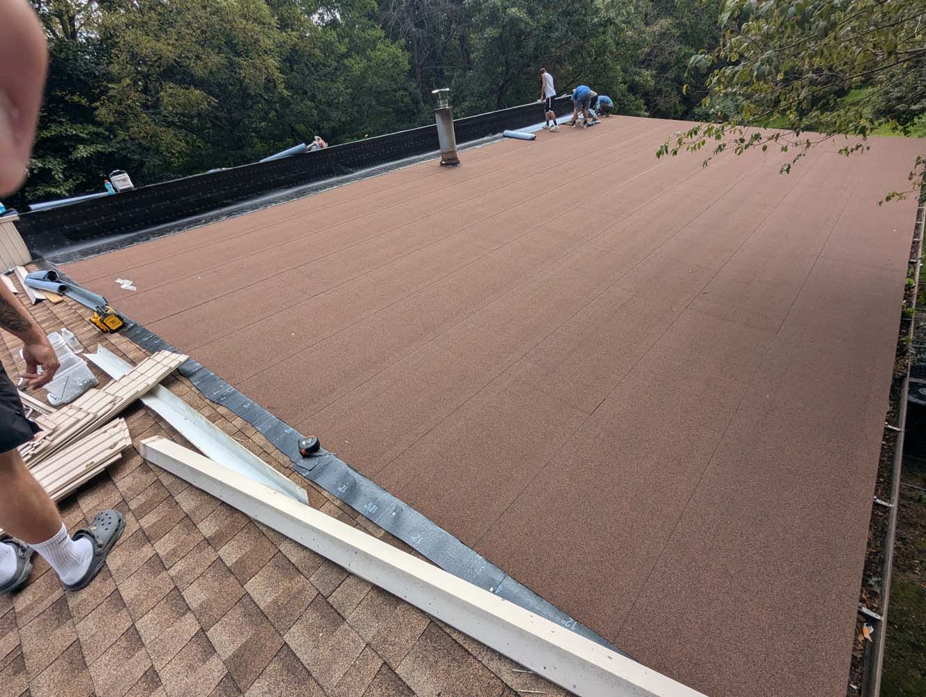 Workers installing a brown, granular roof on a house, tools and materials visible.