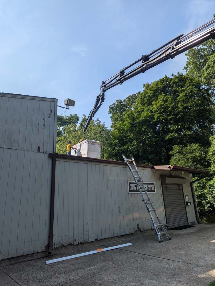 Construction crane over a building, worker on roof. Ladder leans against side. Outdoors on a sunny day.