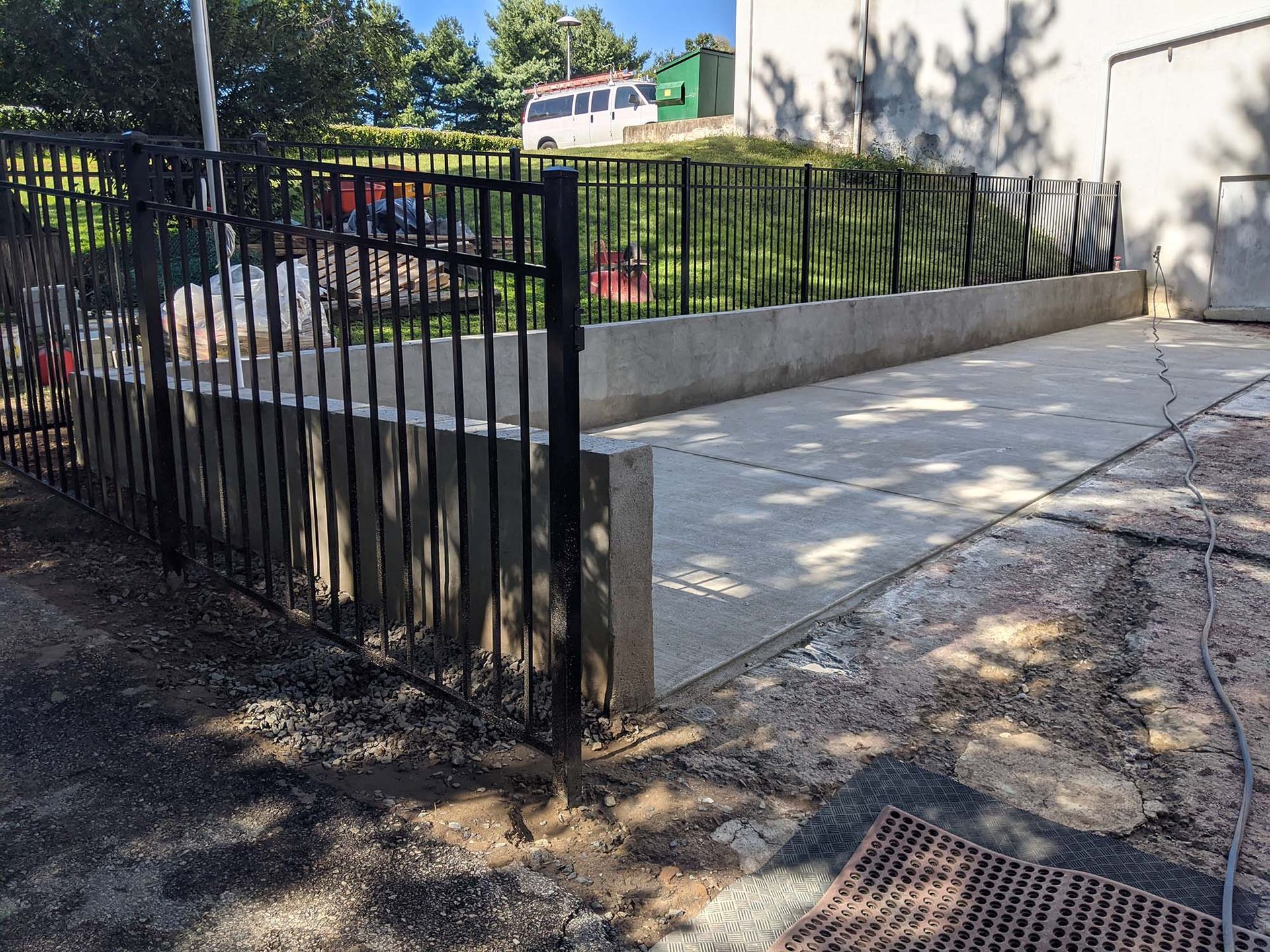 Black metal fence encloses a concrete ramp leading to a green grassy area.