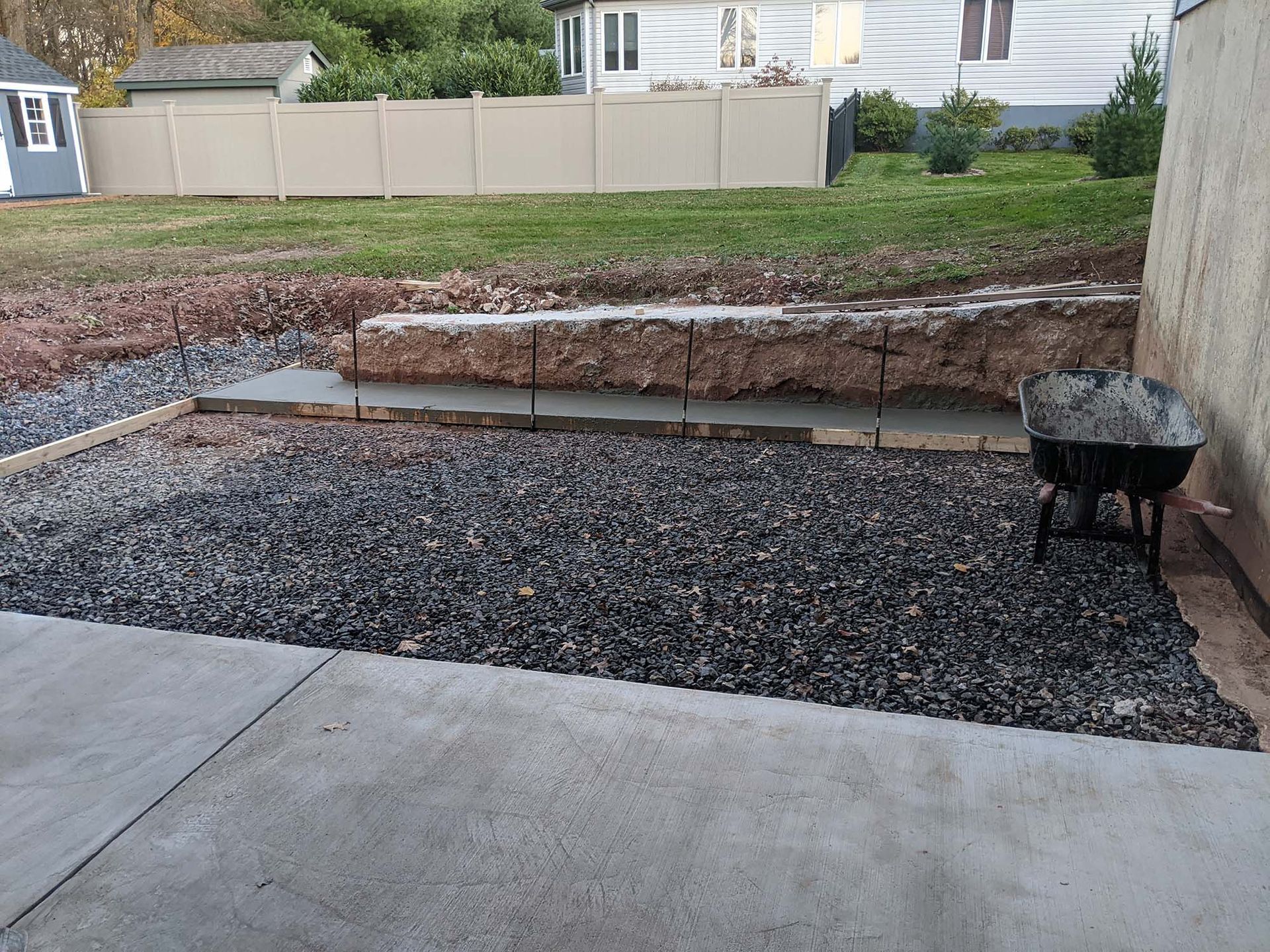 Concrete patio and gravel area being constructed next to a retaining wall and grass.