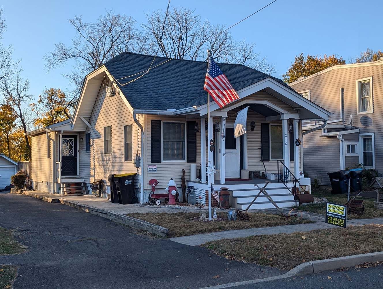 A two-story house with a porch and American flag; driveway and autumn yard.