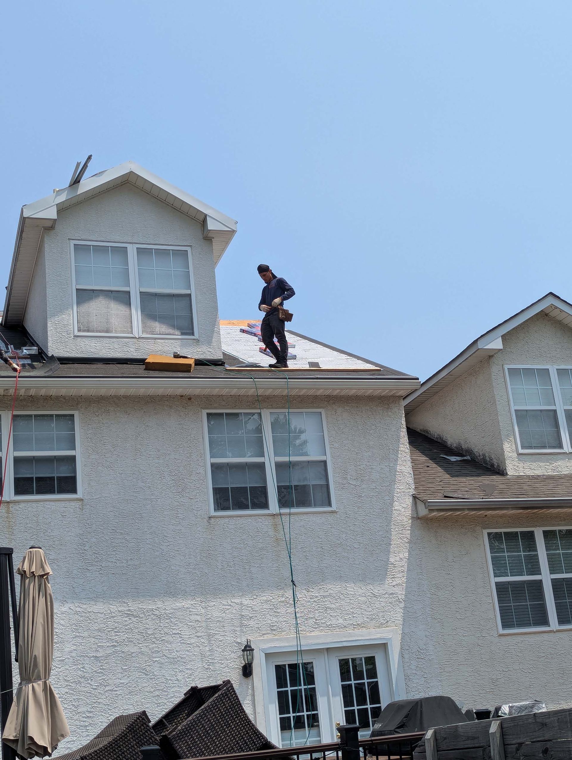 Person on a rooftop of a house, possibly repairing it. Sky is blue, and the house has white stucco siding.