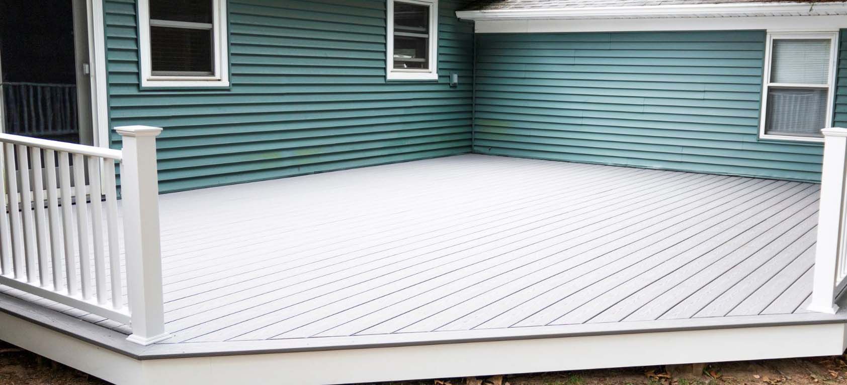 A snow-covered deck with white railing against a teal-sided house.