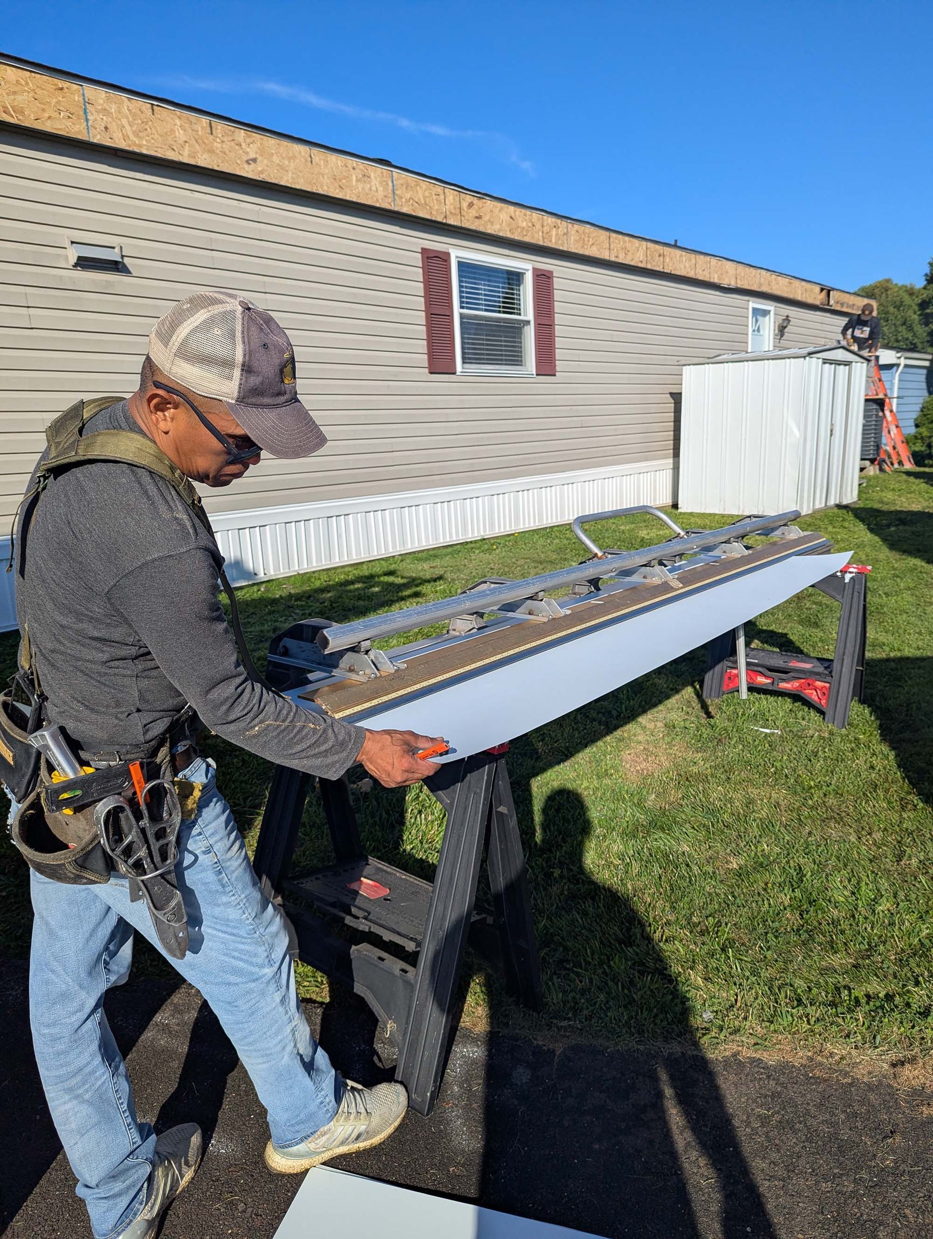 Person holding a piece of siding, preparing to install it on a light-colored mobile home.