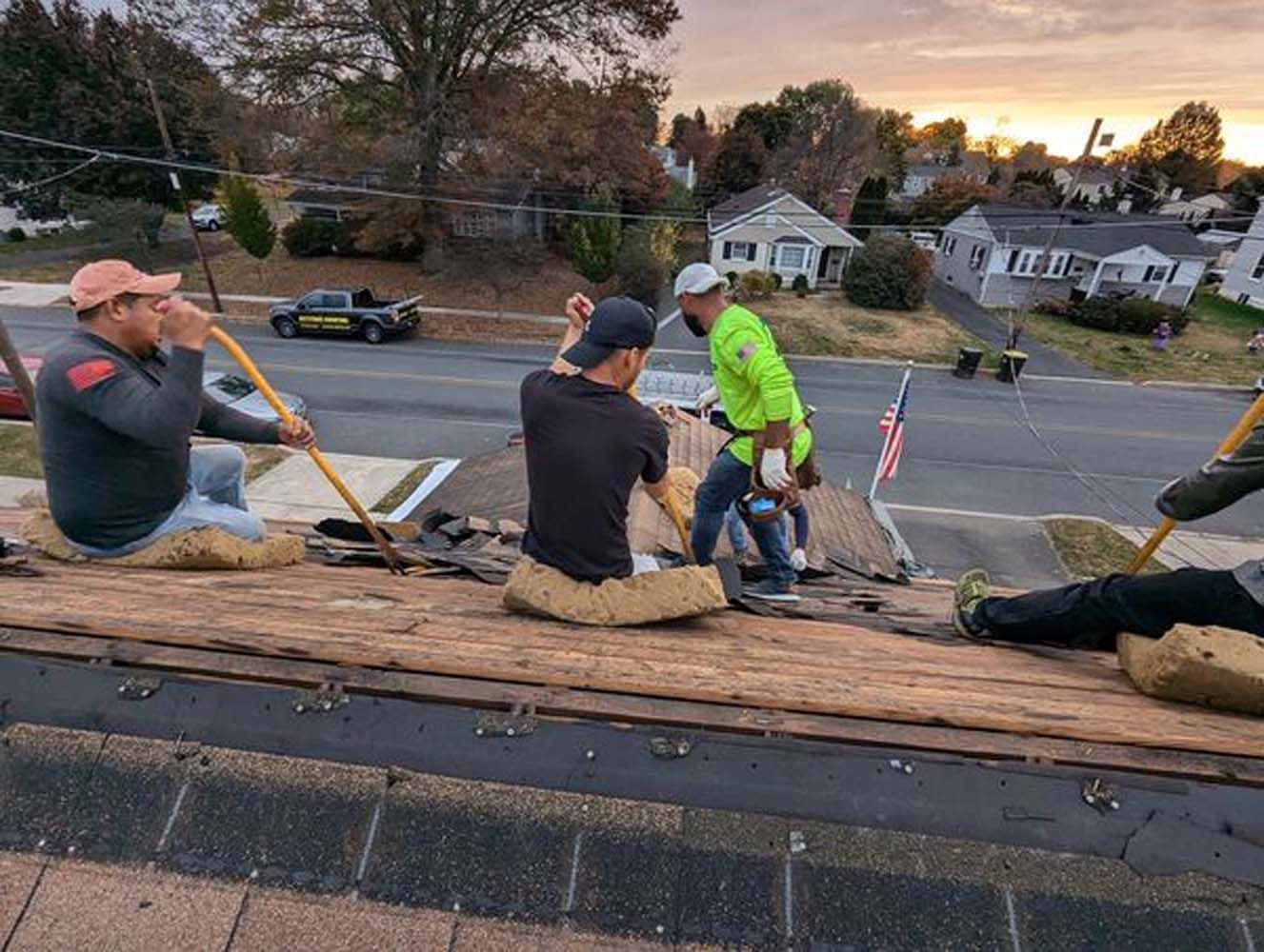 Roofers removing shingles from a house roof on a sunny day.