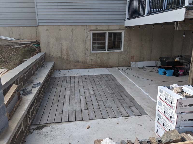 A partially completed patio with brick pavers, near a basement wall and deck.