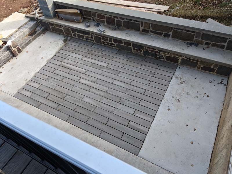Stone patio with brick-like pavers surrounded by concrete and stone walls, likely outdoor.