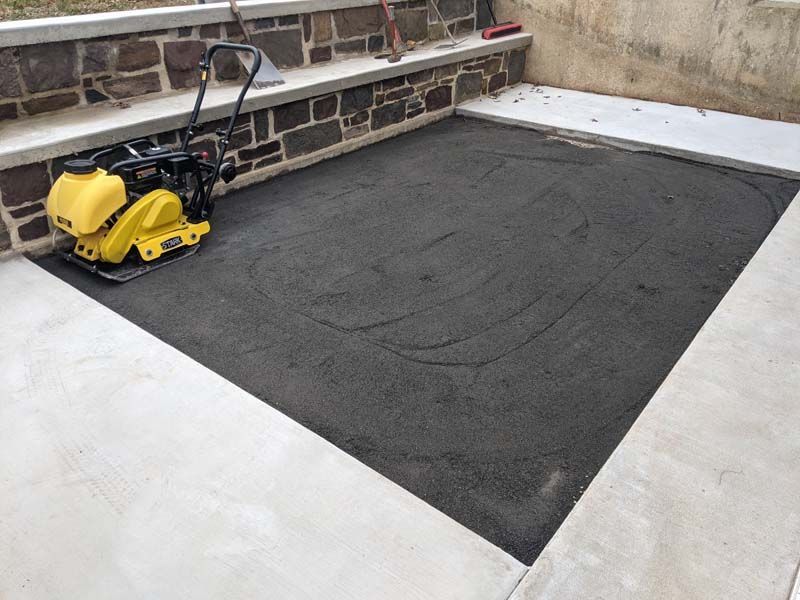 Compactor on fresh asphalt, within concrete border, near stone steps.