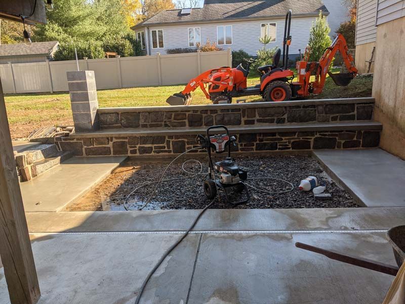 Construction site with concrete patio and stone steps. A small excavator is in the background.