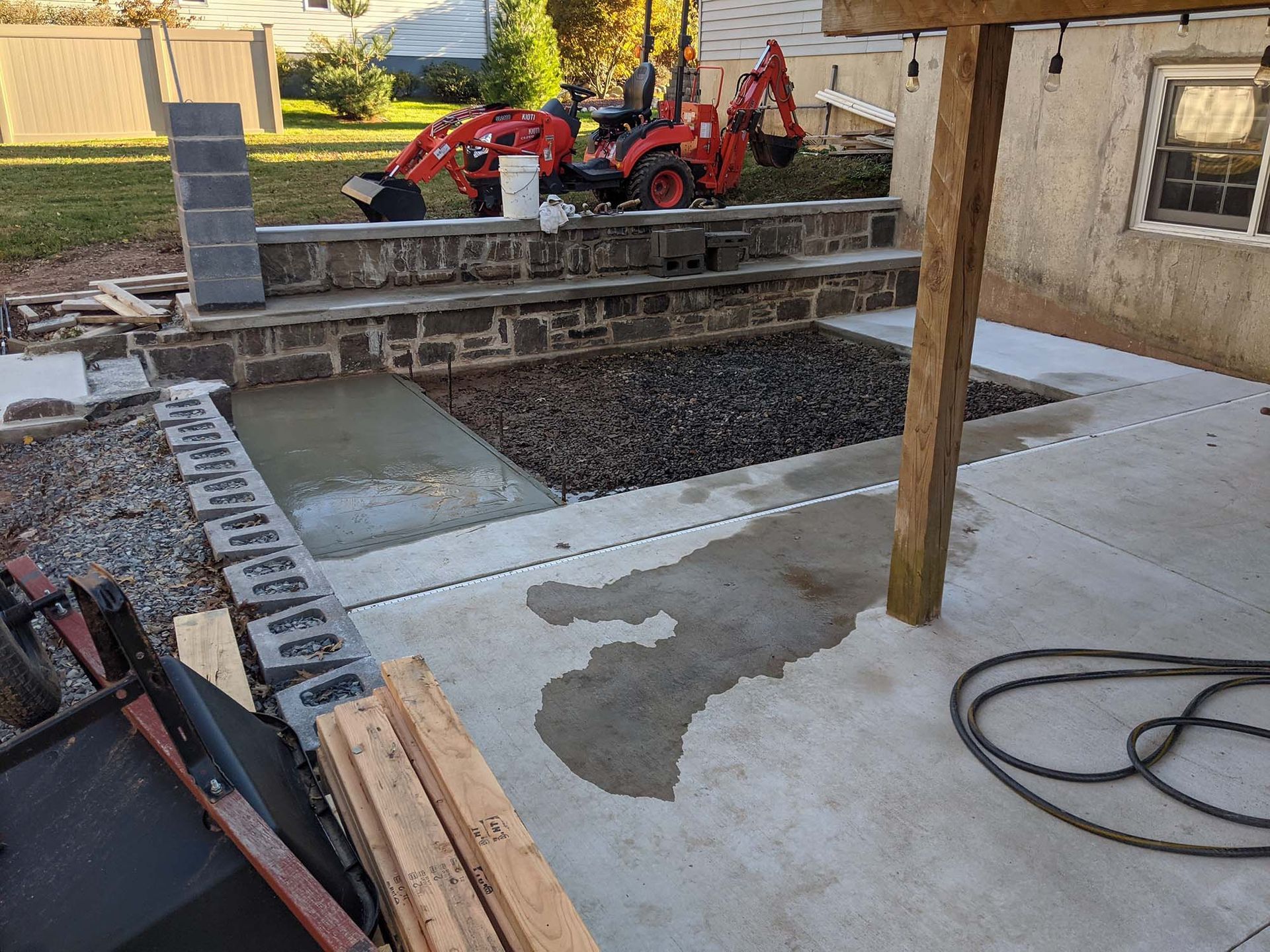 Construction site: backyard patio with concrete, gravel, and stone steps. A small tractor is present.