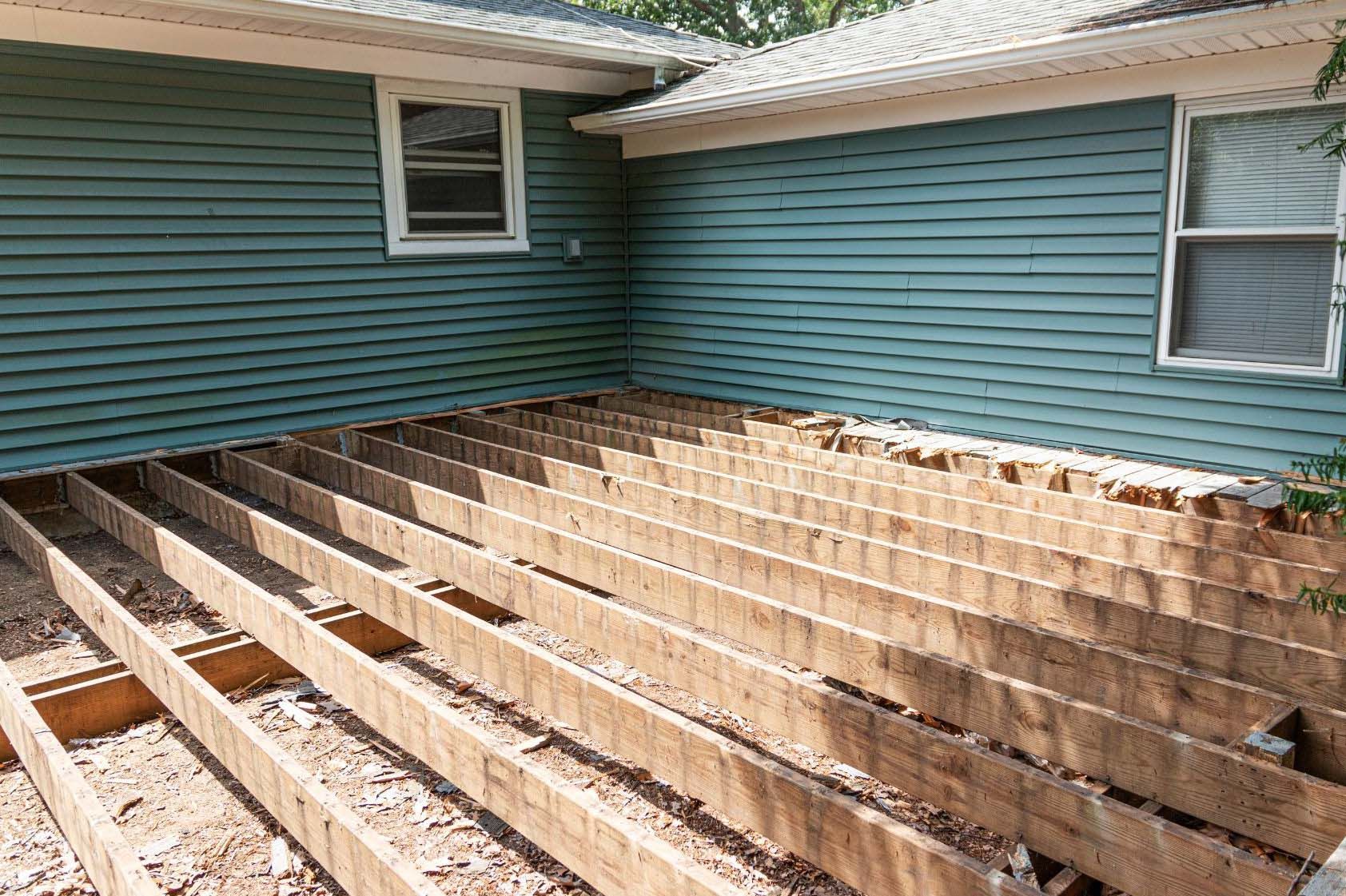 A deck under construction with exposed wooden joists, set against a teal-sided house.