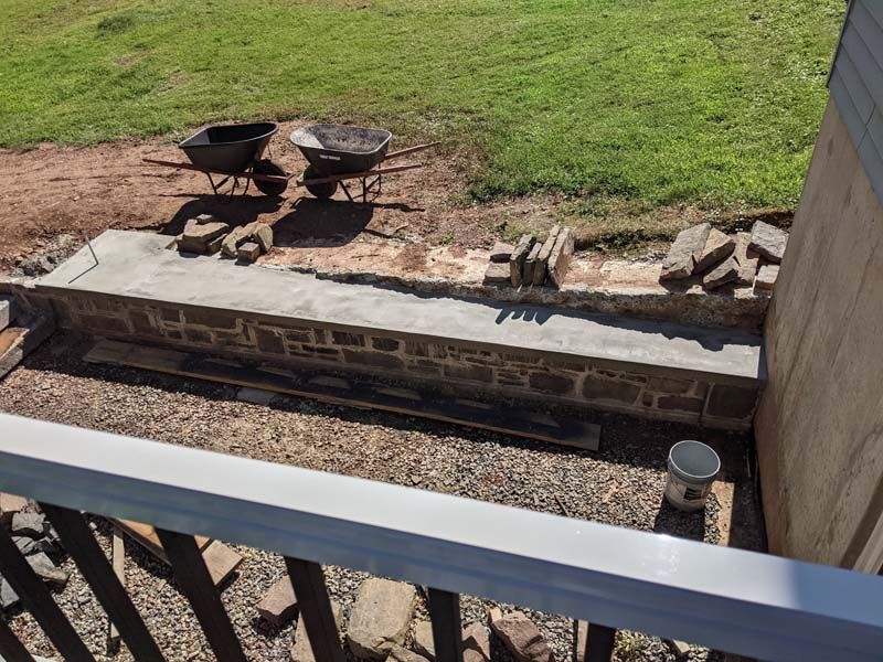 Construction of a low stone wall, with wheelbarrows and grass in the background.