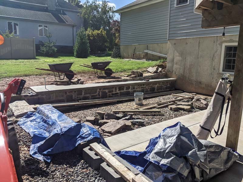 Construction site with stone steps and retaining wall. Wheelbarrows, tarp, and building materials are present.