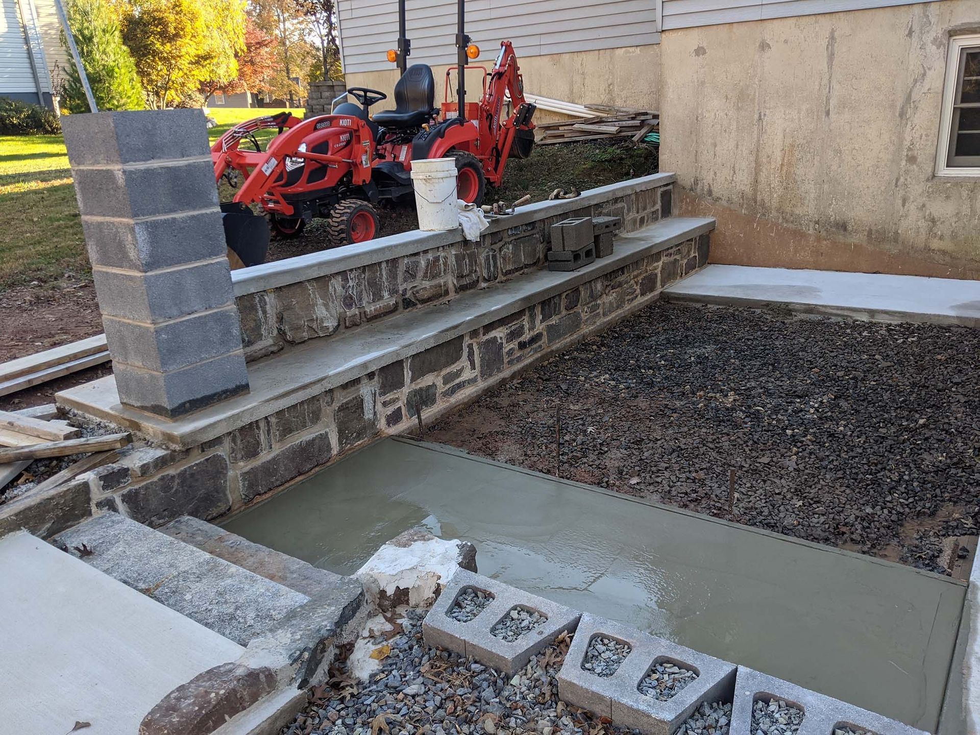 Concrete steps and retaining wall under construction next to a house, with a red tractor visible.