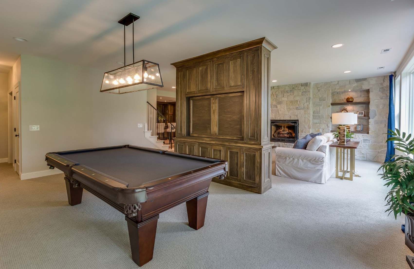 Pool table in a game room with fireplace and seating area. Brown wood paneling. Light-colored carpet.