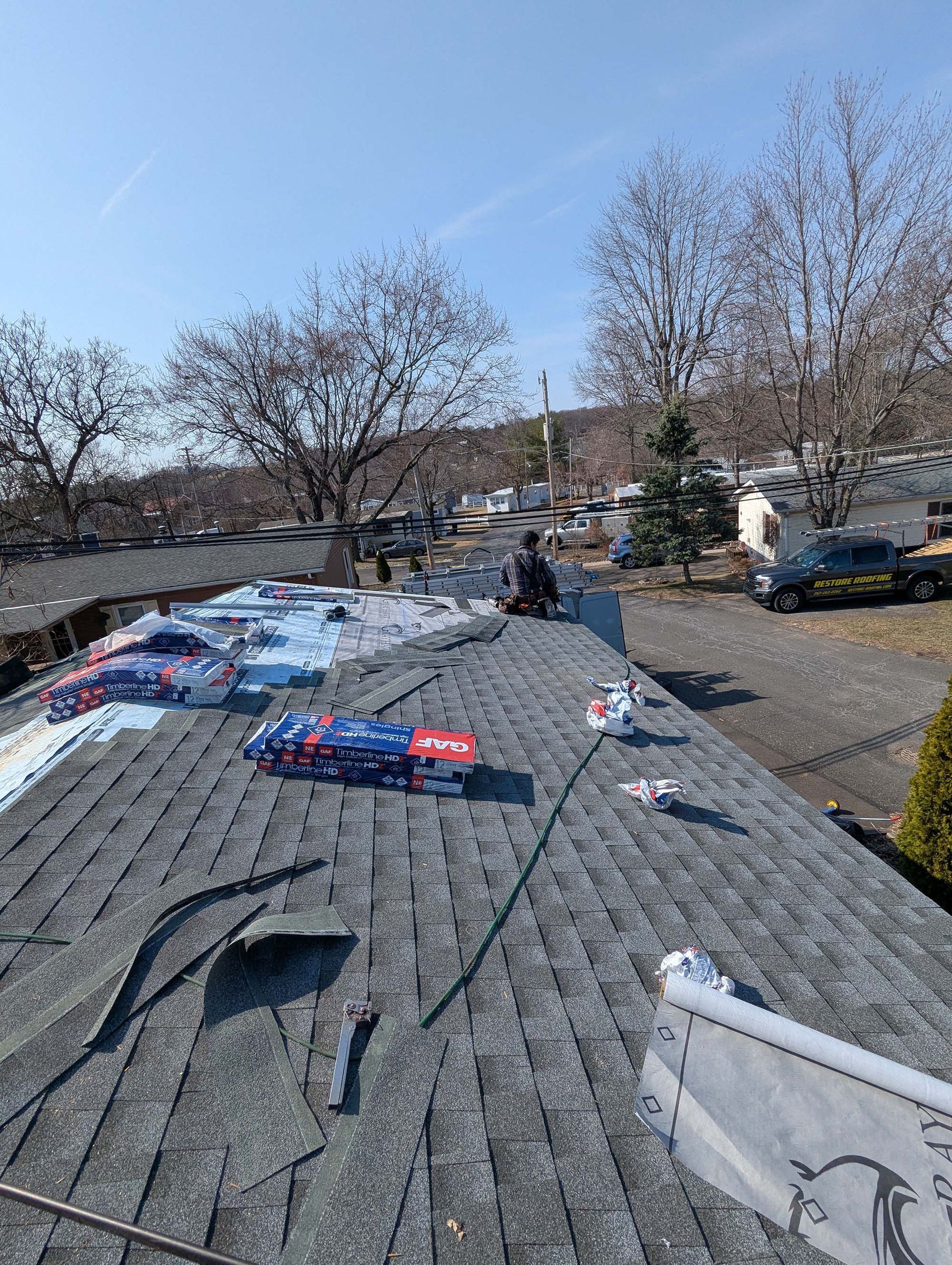 Workers installing shingles on a roof on a sunny day.