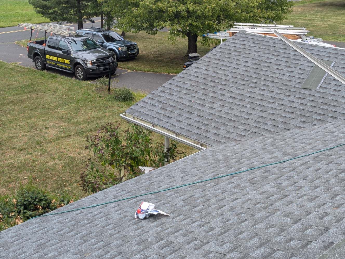 Gray shingled roof with a small toy on it, work trucks in the background.