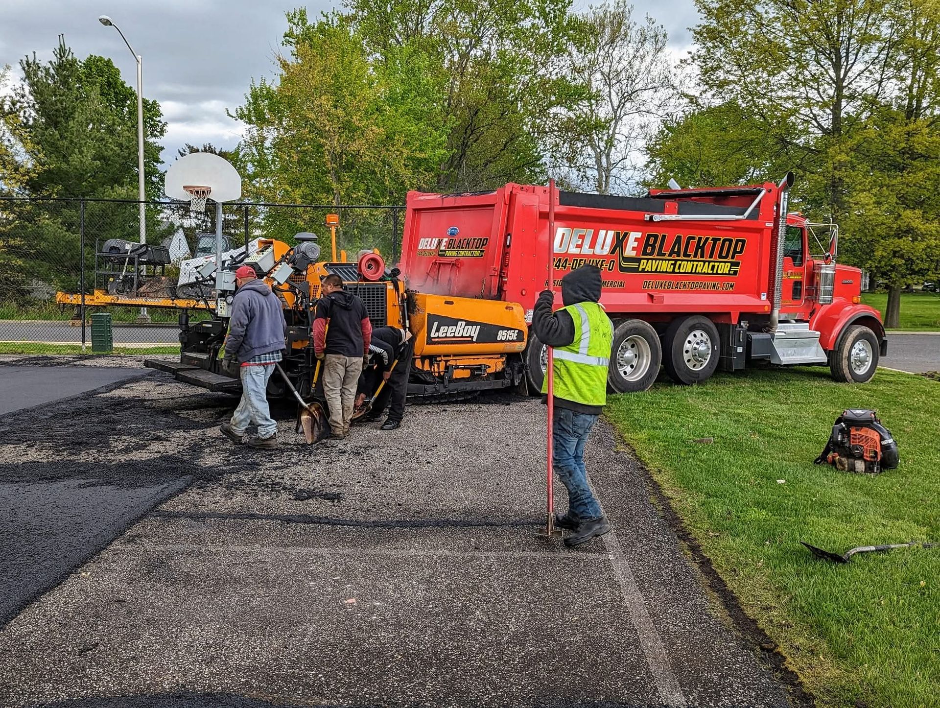 Asphalt paving crew at work, using machinery to lay fresh asphalt road. Red dump truck nearby.
