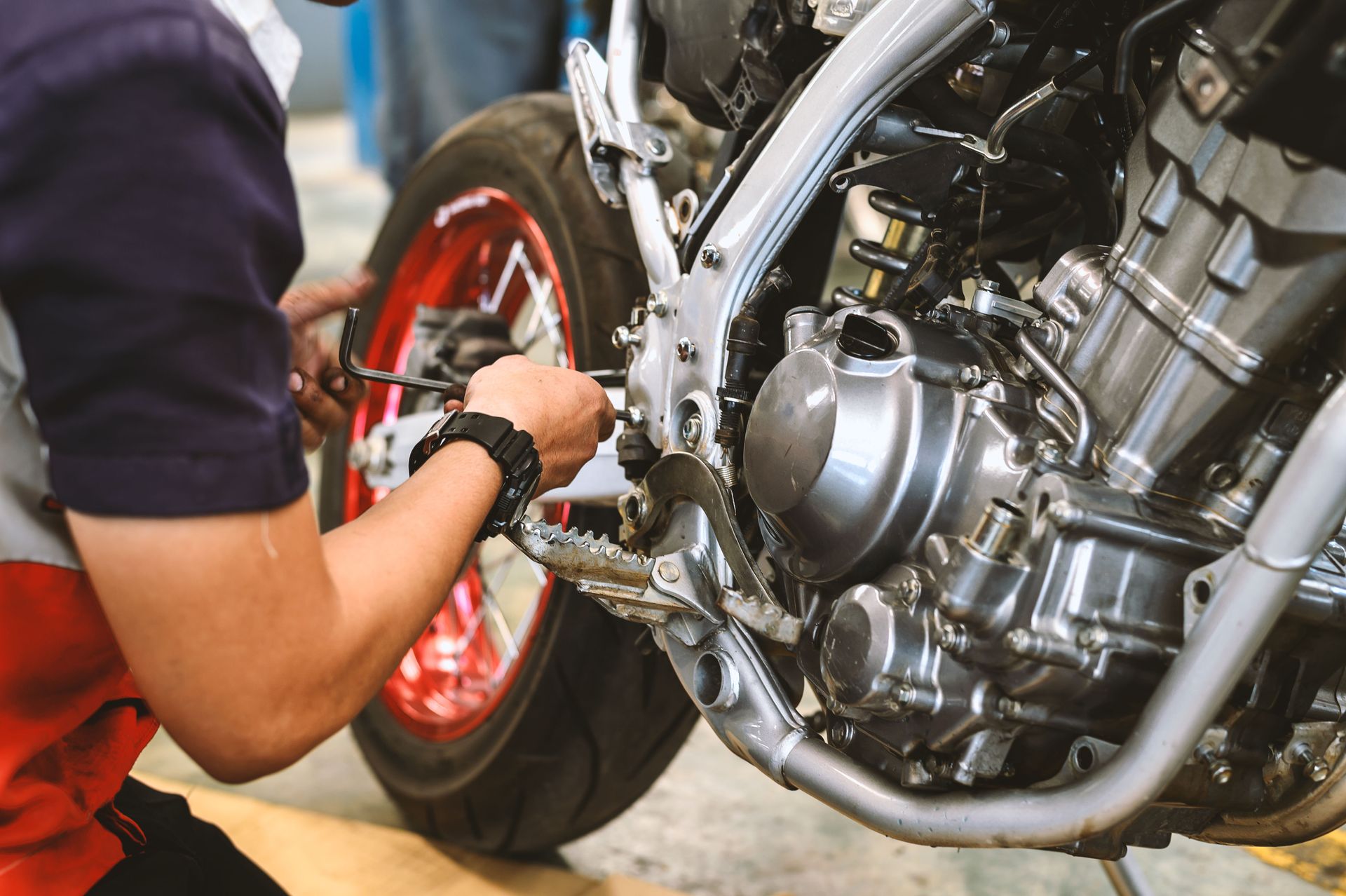 Mechanic working on a motorcycle engine. They use a wrench near the tire and chain in a garage setting.