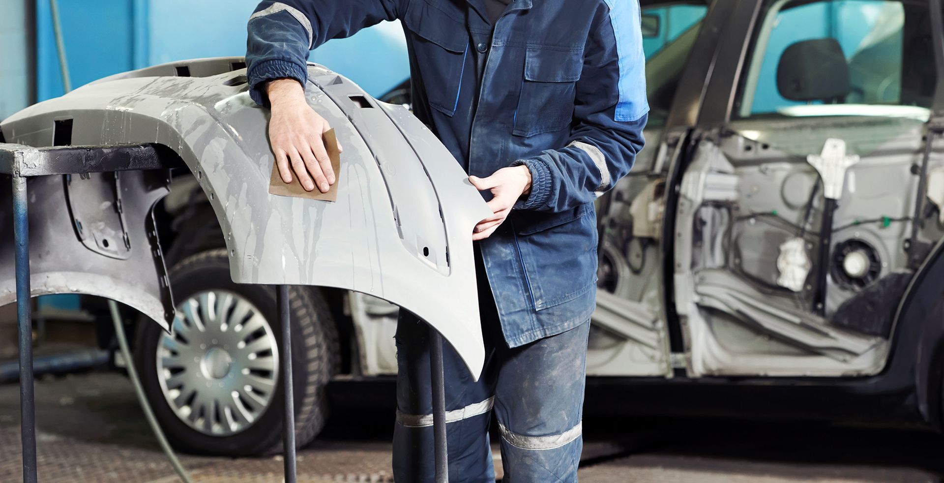 Mechanic sanding a car fender in a repair shop.