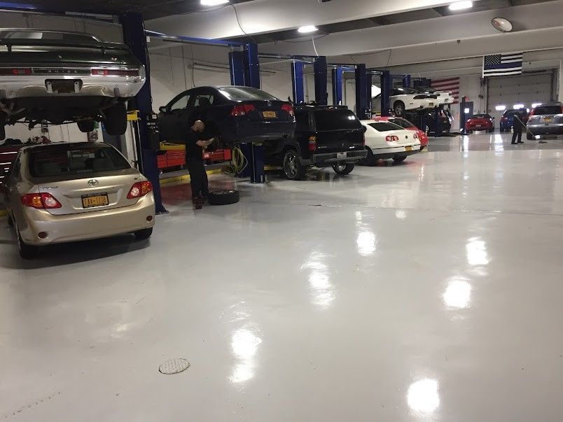 Cars on lifts in a brightly lit auto repair shop, a mechanic working.