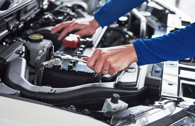 Hands of a mechanic working on a car engine, likely inspecting the battery.