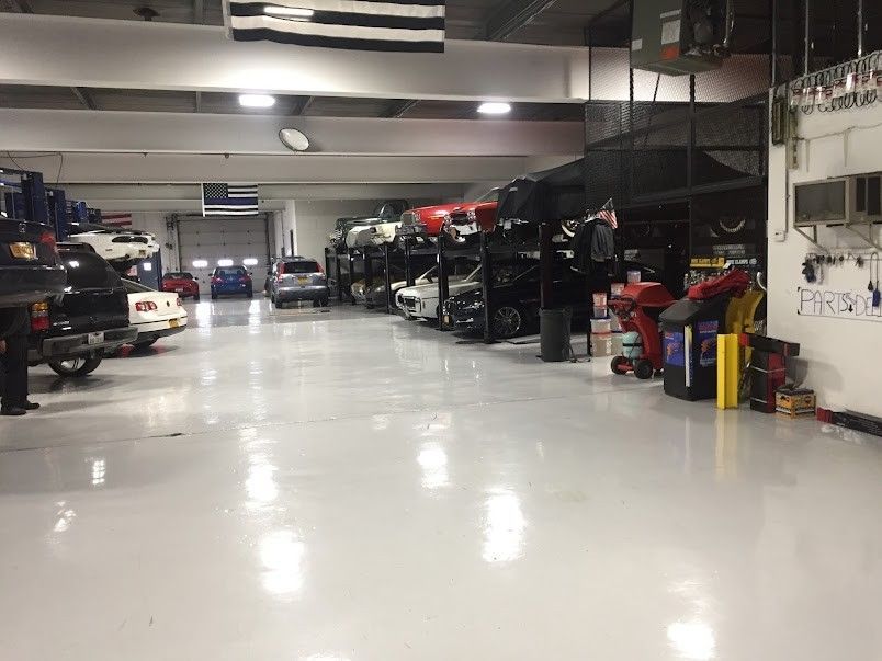 A car repair shop with multiple vehicles on lifts. The floor is light grey, and the shop is well-lit.